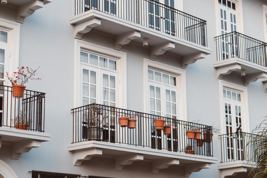 Front view of a modern building with balconies, pots, and white framed windows.