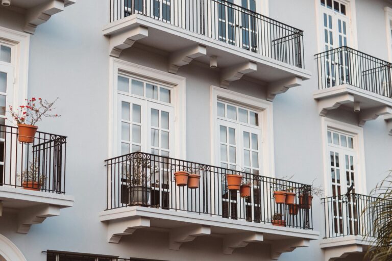 Front view of a modern building with balconies, pots, and white framed windows.