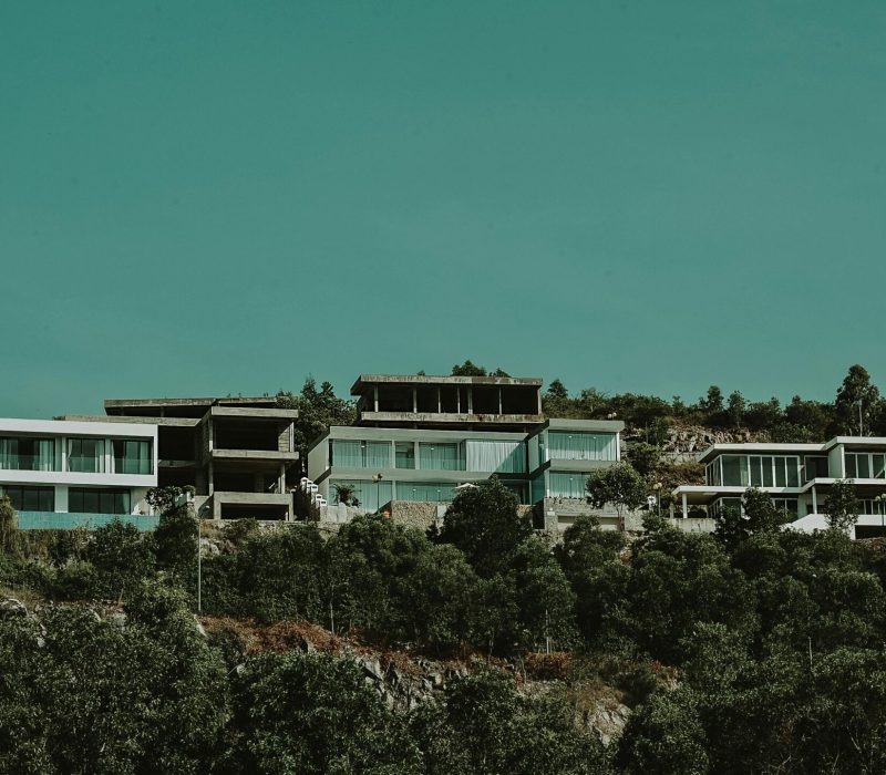 Contemporary hillside villas surrounded by lush greenery under an expansive sky.
