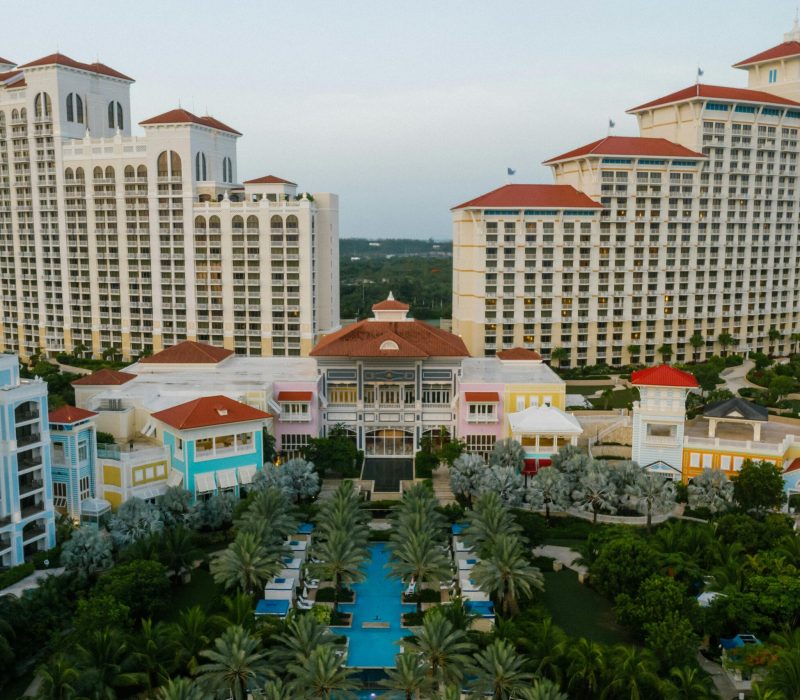 Aerial view of a luxury resort with high-rise towers, palm trees, and a central swimming pool.